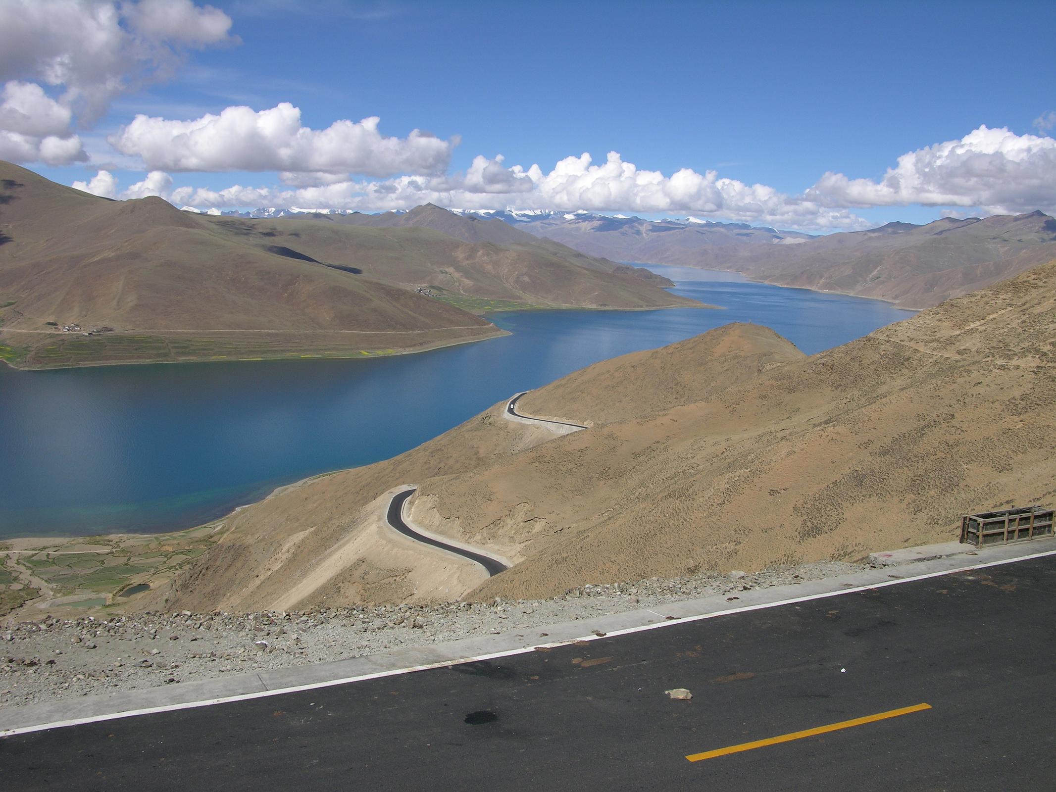 Tibet 05 01 Yamdrok Tso Kamba La The road from Lhasa to Gyantse (260km) took us over two mountain passes. From the Kamba La (4794m), we had a fantastic view of the beautiful Yamdrok Tso (Turquoise lake) with Nojin Kangtsang (7191m) behind, hidden in the clouds. In the foreground is the new paved road just opened in June 2005, in preparation for the 40th anniversary of the creation of the Tibet Autonomous Region.